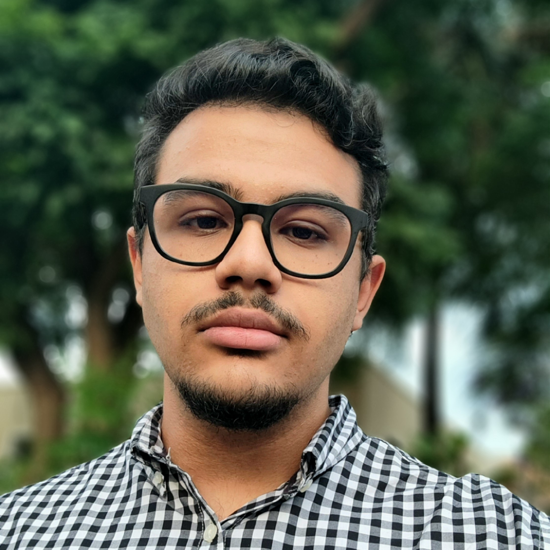 My selfie, background has some trees, i'm with a serious look, wearing a black rounded glasses